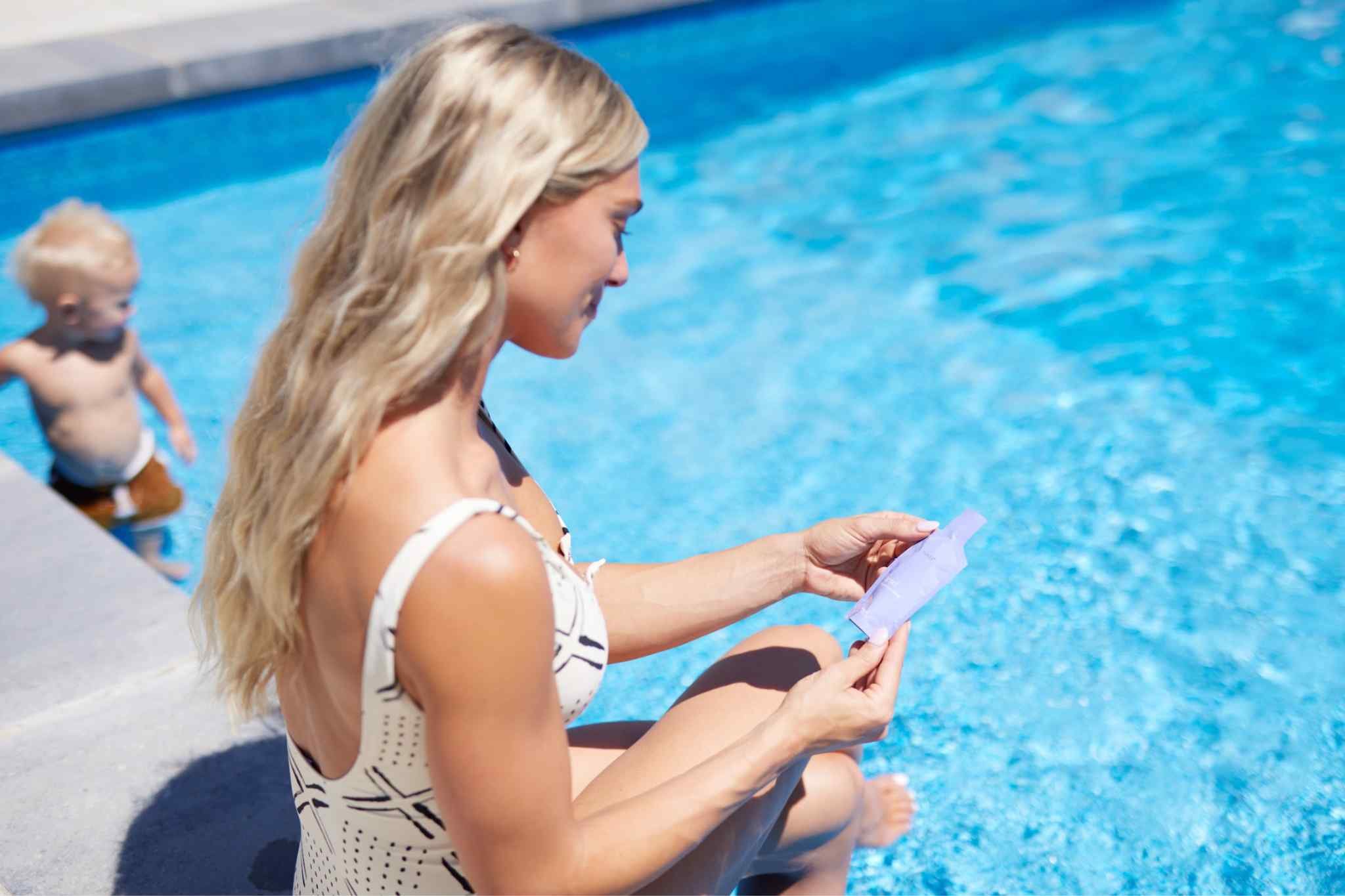 Woman sitting poolside holding an Éternel Antioxidant Super-Blend pouch as part of her everyday wellness routine.