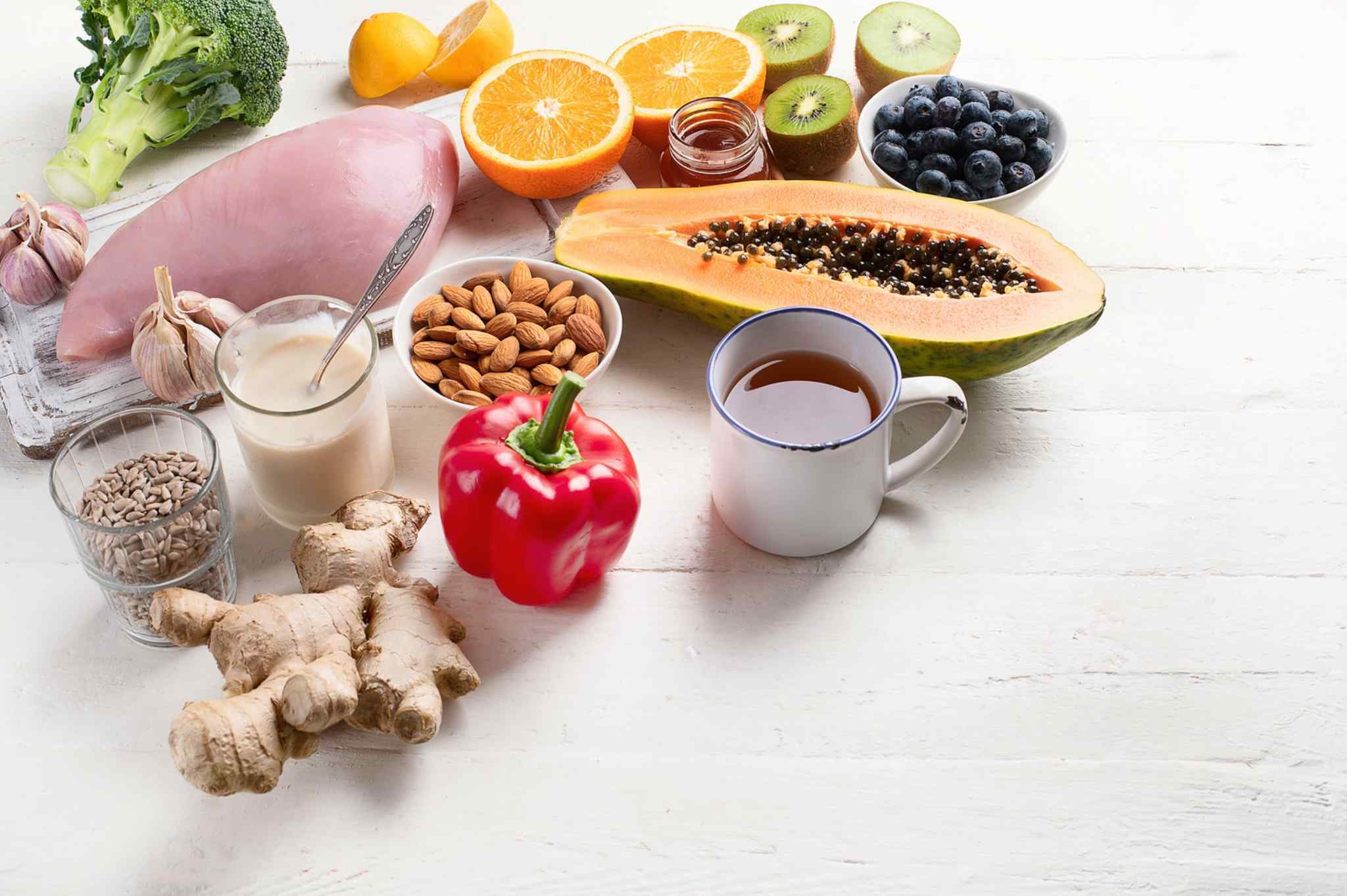 Colorful nutrient-rich foods including citrus, kiwi, blueberries, broccoli, almonds, ginger, papaya, and other sources of vitamins and minerals that support healthy immune function.
