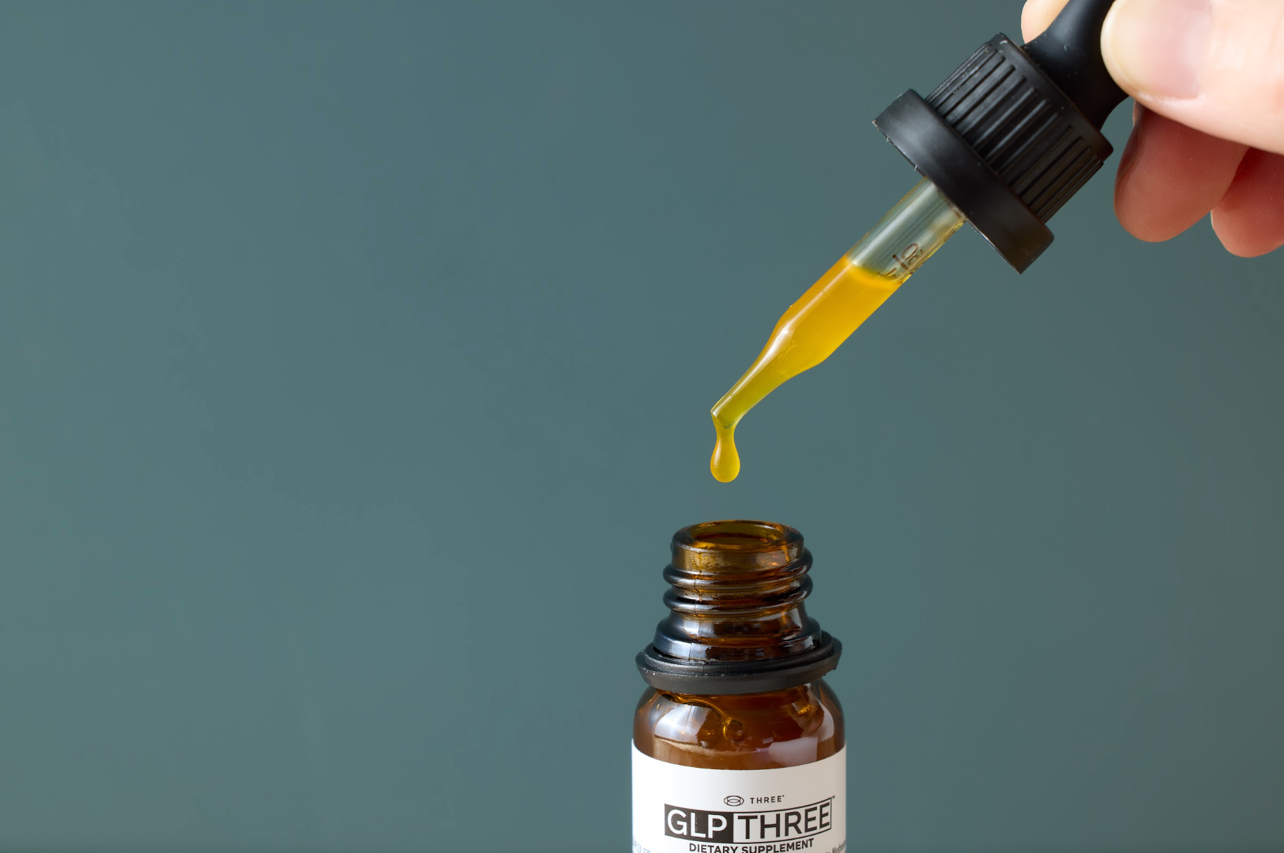 A dropper filled with GLP THREE liquid positioned above the supplement bottle. GLP THREE combines natural peptides and botanical ingredients in a liquid formula designed to support appetite awareness and metabolic wellness.