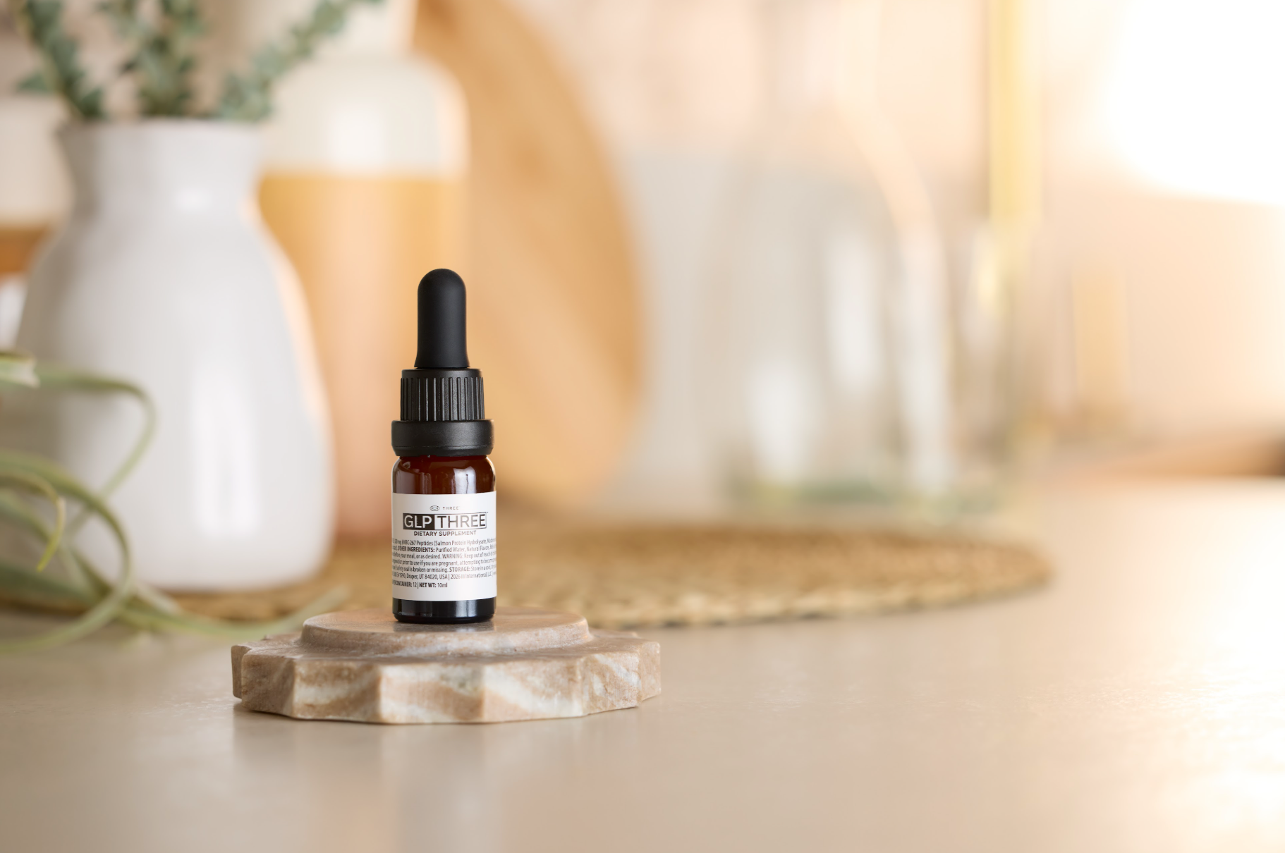 A bottle of THREE GLP THREE displayed in a bright wellness setting. The nutrition-based supplement is formulated to provide natural GLP-1 support for appetite awareness, healthy weight management, and metabolic wellness.