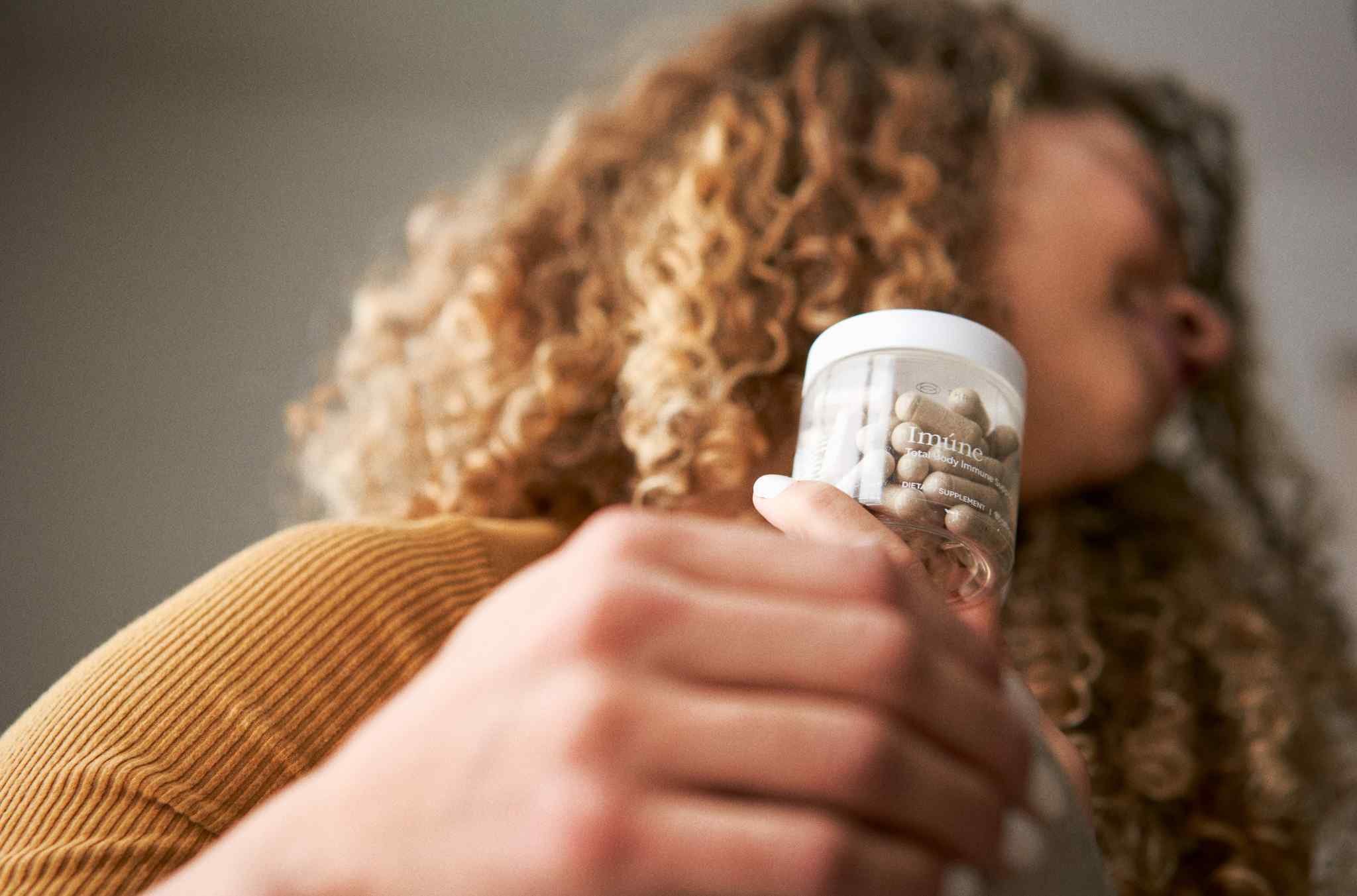 Woman holding a bottle of THREE Imúne Total Body Immune Support. Imúne combines plant-based compounds with complementary nutrients in a daily formula designed to support immune health.