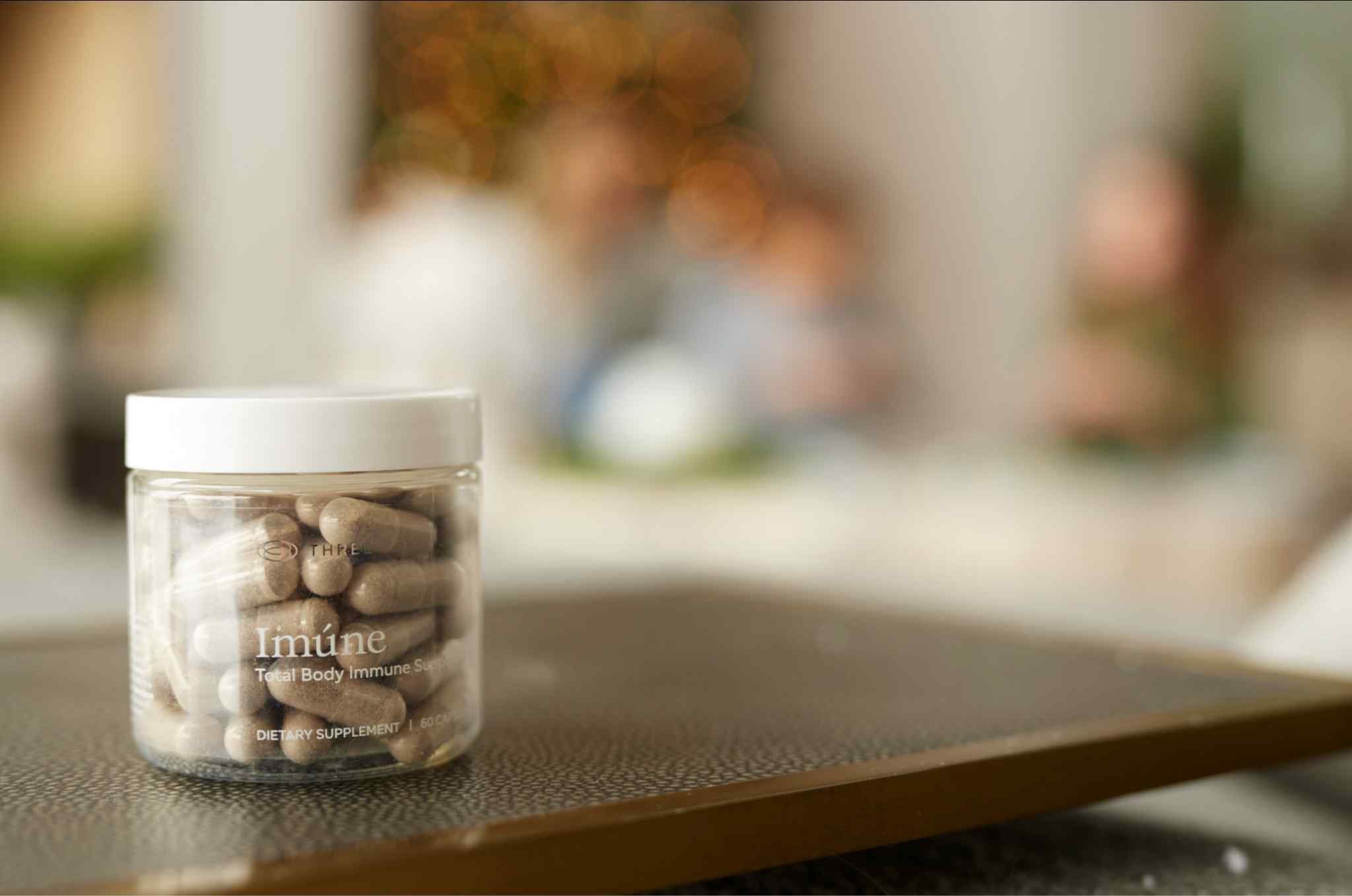 Bottle of Imúne Total Body Immune Support capsules displayed in a home setting, featuring THREE’s comprehensive daily immune support formula.