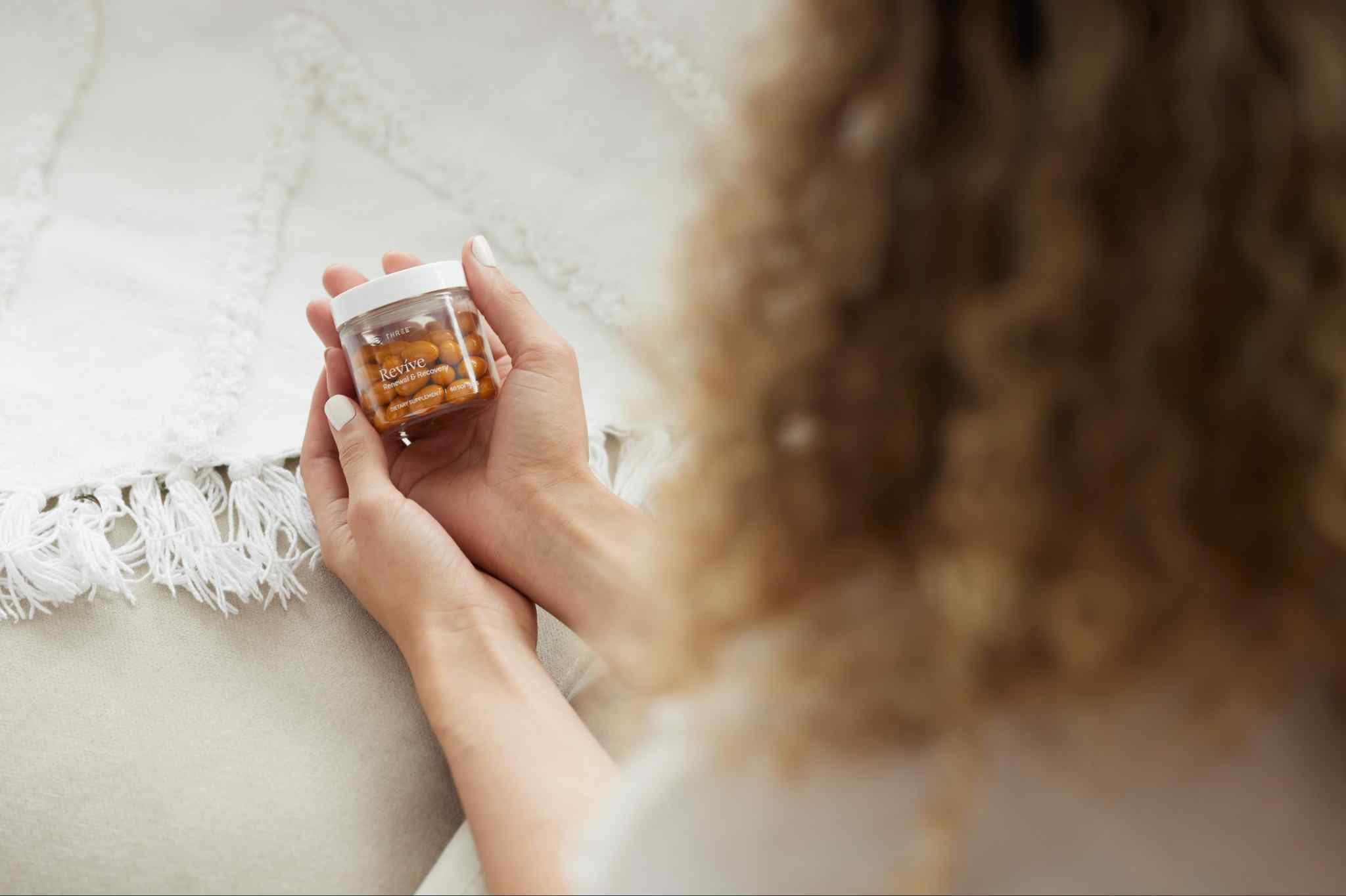 Woman holding a bottle of THREE Revíve Renewal & Recovery, a joint support supplement formulated with Boswellia and complementary compounds to support mobility and joint wellness.