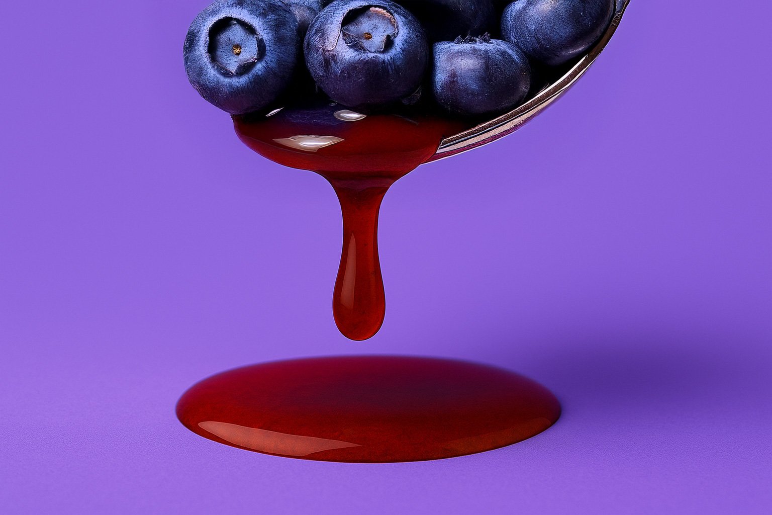 Close-up of fresh blueberries on a spoon with antioxidant-rich juice dripping into a pool, symbolizing the vibrant phytonutrient power of resveratrol found in Èternel.
