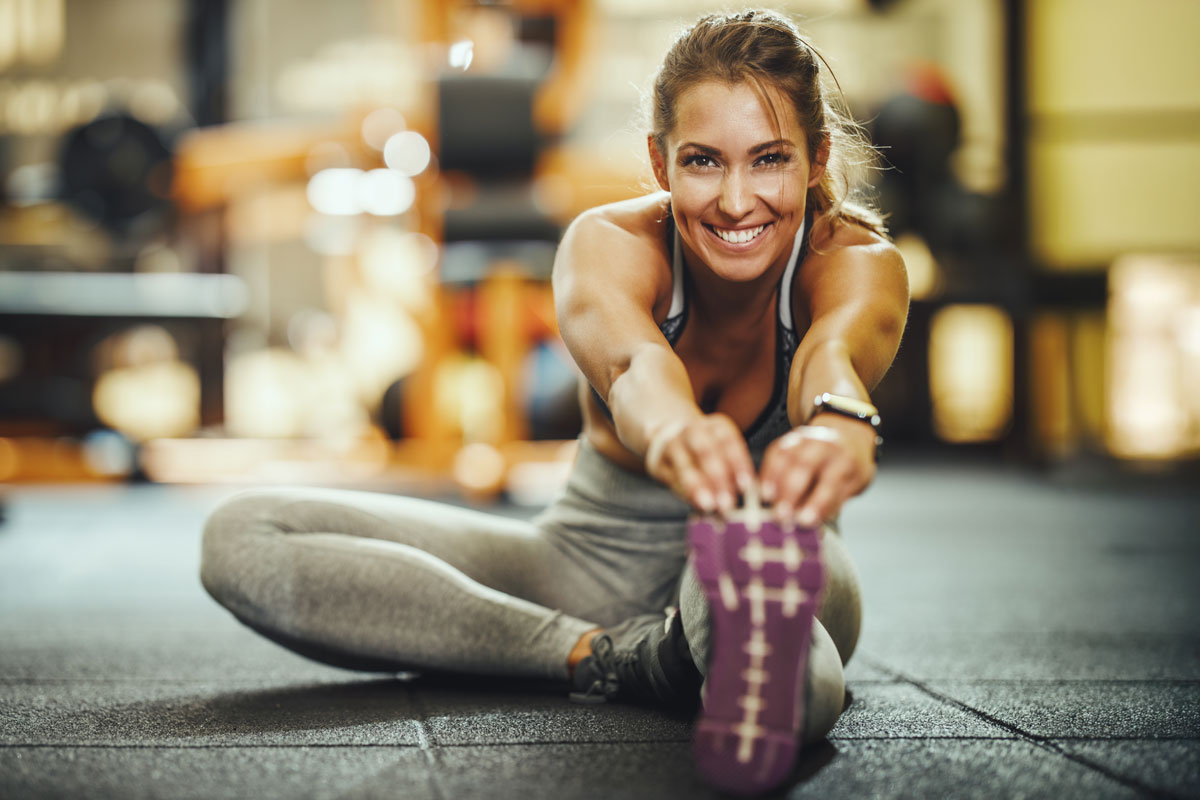 woman stretching at the gym and smiling at the camera