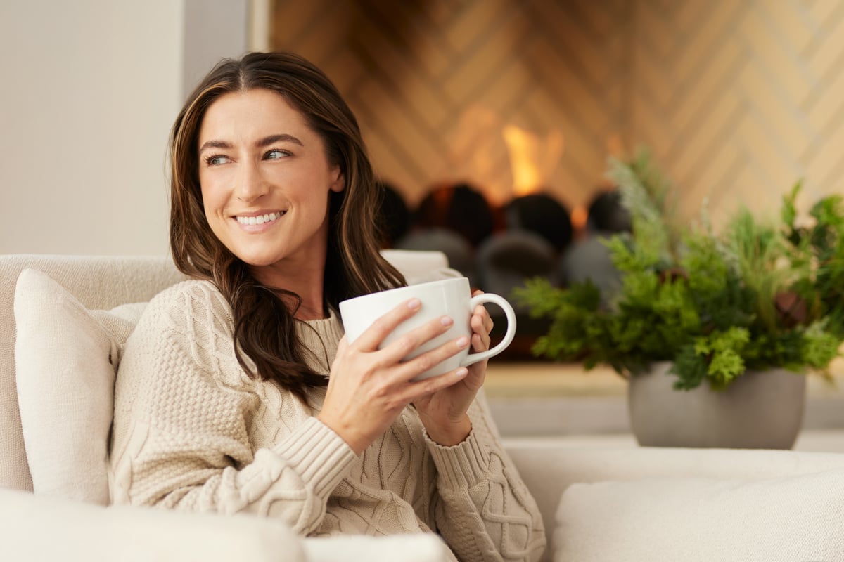 woman sitting next to a fire with a cup of coffee smiling during the holidays