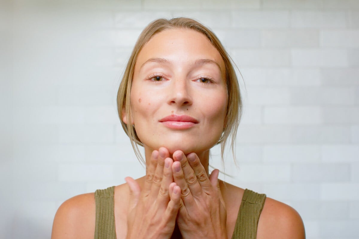 A woman admiring her radiant skin after applying Visage Super Serum by THREE