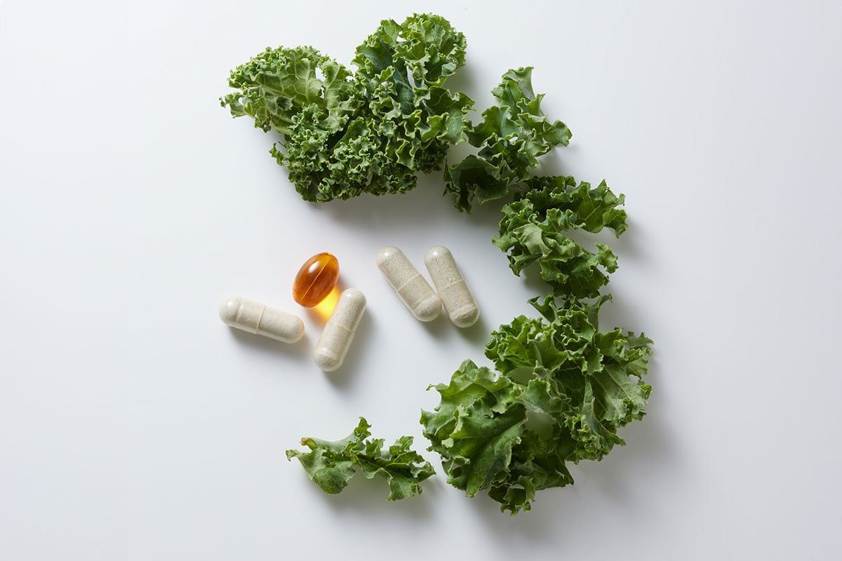 Vitalité by THREE supplement sitting next to fresh kale